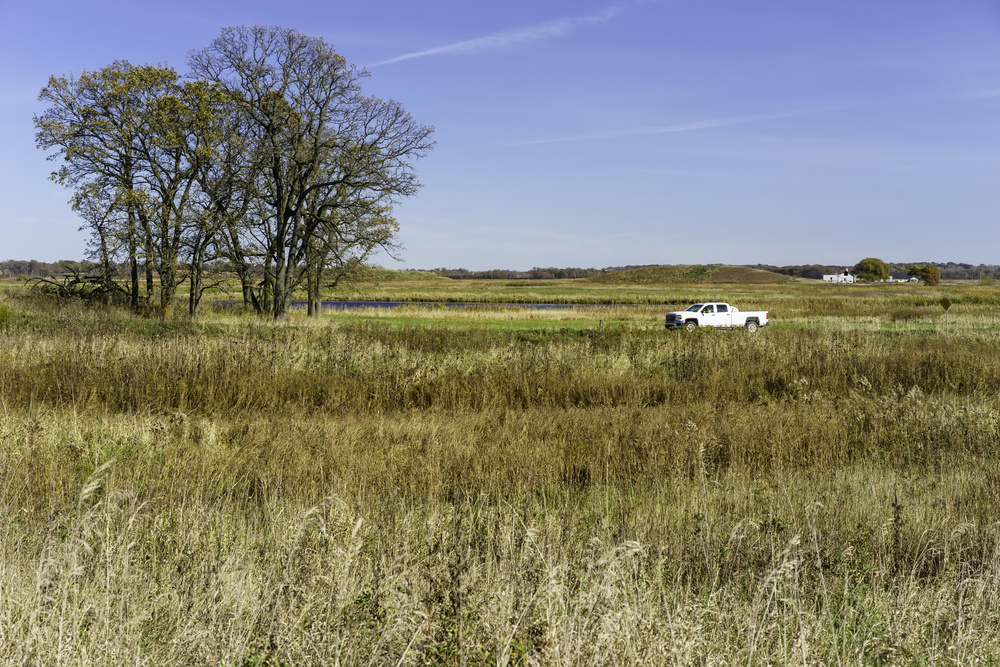 Pickup truck with unidentifiable driver passing by a kame (a hill created by a glacial deposit)  in northern Illinois, USA, in fall, for themes of travel, transportation, conservation on public lands